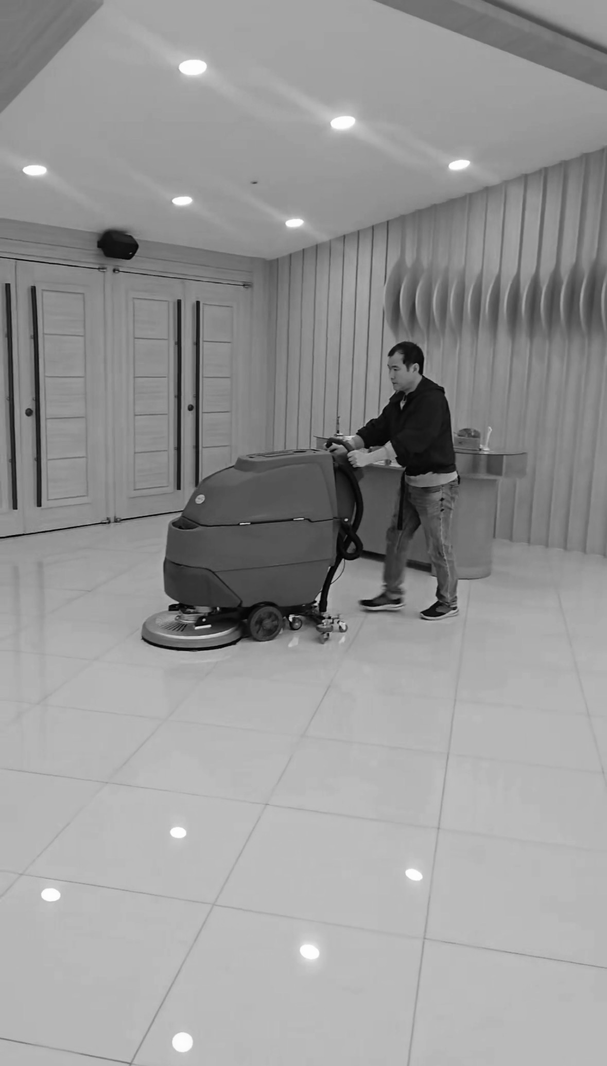 넓은 로비에서 바닥 청소 장비로 작업하는 이훈 대표의 흑백 사진